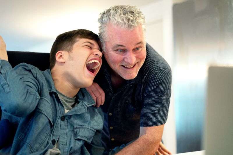 Ein Heilpädagoge und ein Junge mit Behinderung lachen herzlich.